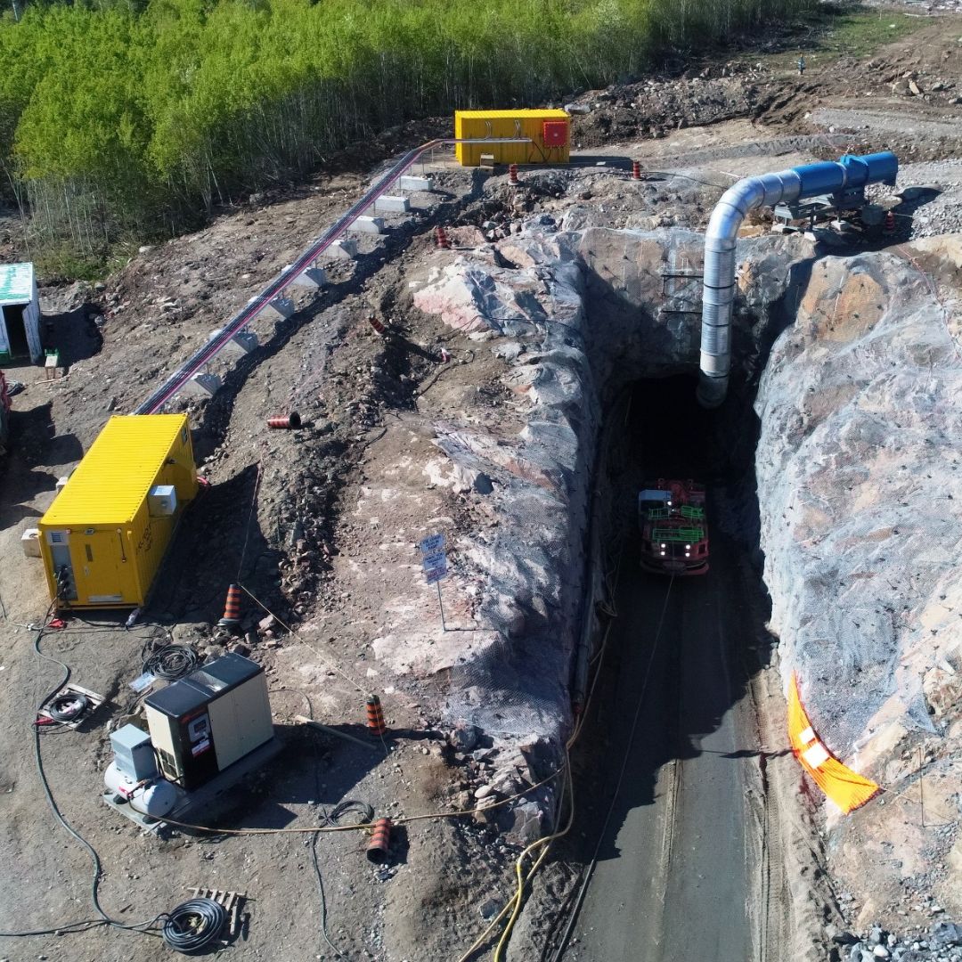 Caron Equipment Aerial view of a large tunnel entrance at a mine site construction area with equipment, vehicles, and ventilation systems from Caron Equipment clearly visible.