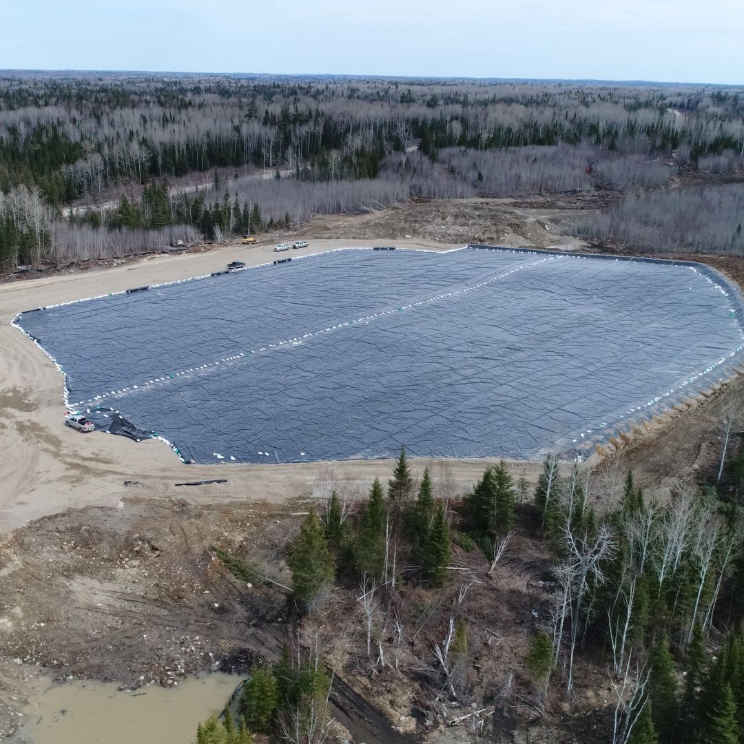 Caron Equipment Aerial view of a large, covered rectangular area in a clearing surrounded by leafless and evergreen trees. Vehicles and equipment from Caron Equipment, specialists in mine site construction, are visible nearby.