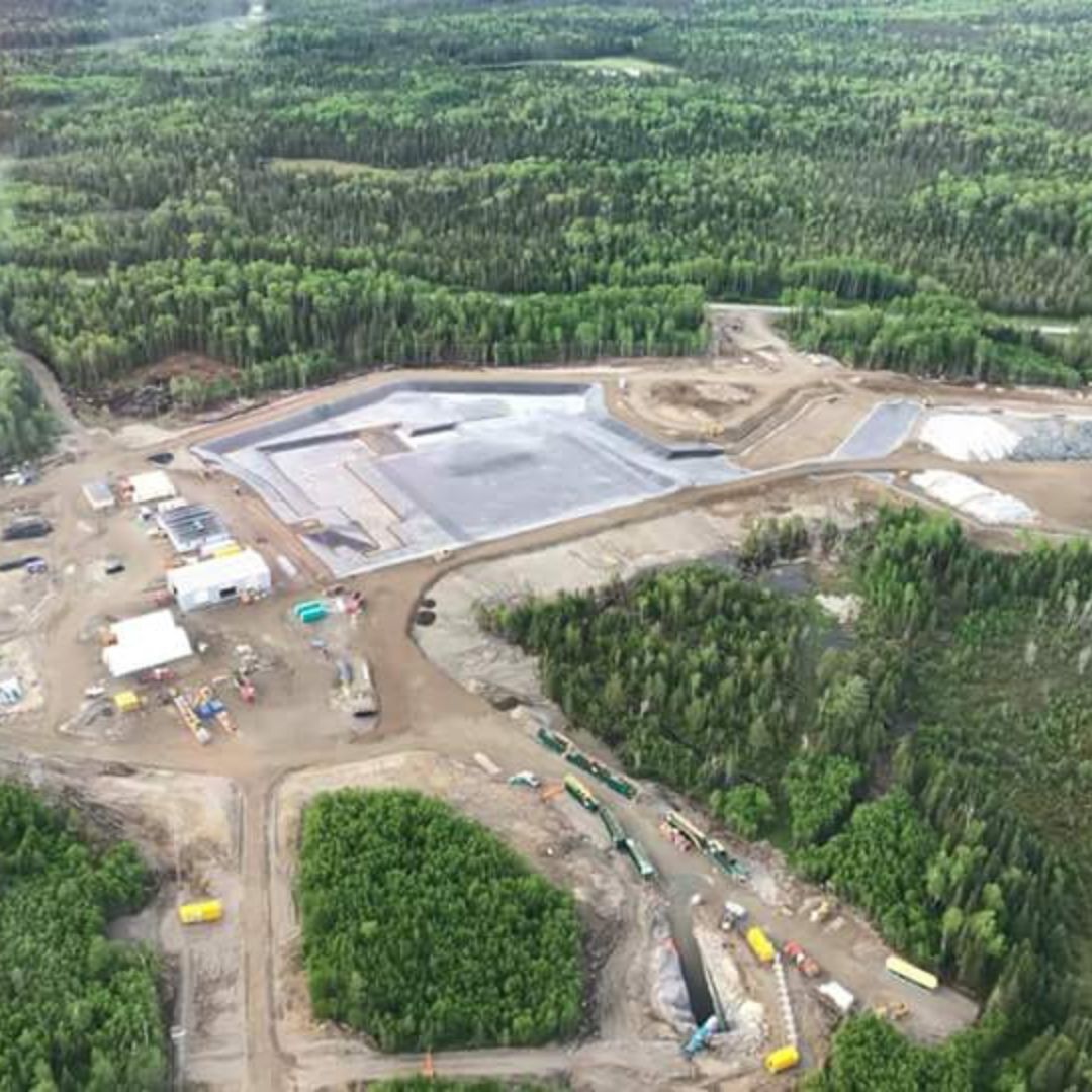 Caron Equipment Aerial view of a construction site surrounded by dense forest, showcasing cleared land, a large foundation, vehicles from Caron Equipment, and temporary structures—perfectly illustrating the meticulous process of mine site construction.