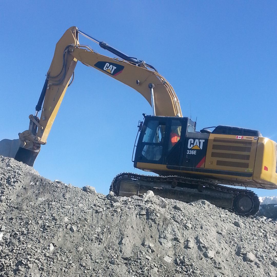 Caron Equipment A yellow CAT 336E excavator from Caron Equipment is expertly positioned on a rocky hill under a clear blue sky, showcasing its expertise in mine site construction.