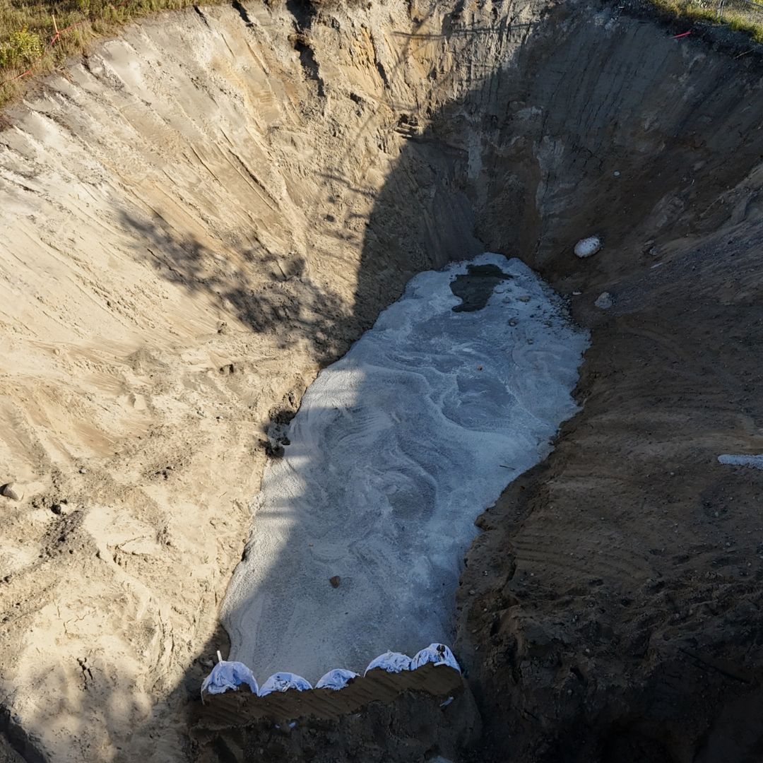 Caron Equipment The large, empty pit with sloping, sandy walls resembles a scene from a civil construction project. Its bottom displays a light-colored, powdery texture, typical of mine site construction. Top edges of sandbags are visible near the lower edge of the pit.