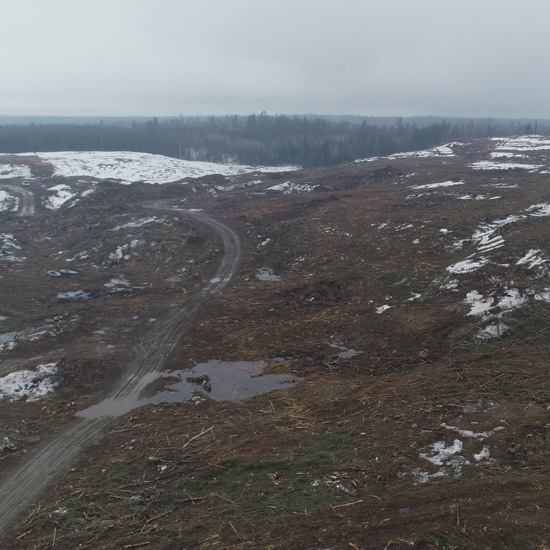 Caron Equipment A barren landscape with dirt roads and patches of snow under a cloudy sky, surrounded by sparse trees in the distance, hints at ongoing civil construction—perhaps a Caron Equipment mine site construction shaping the rugged terrain.