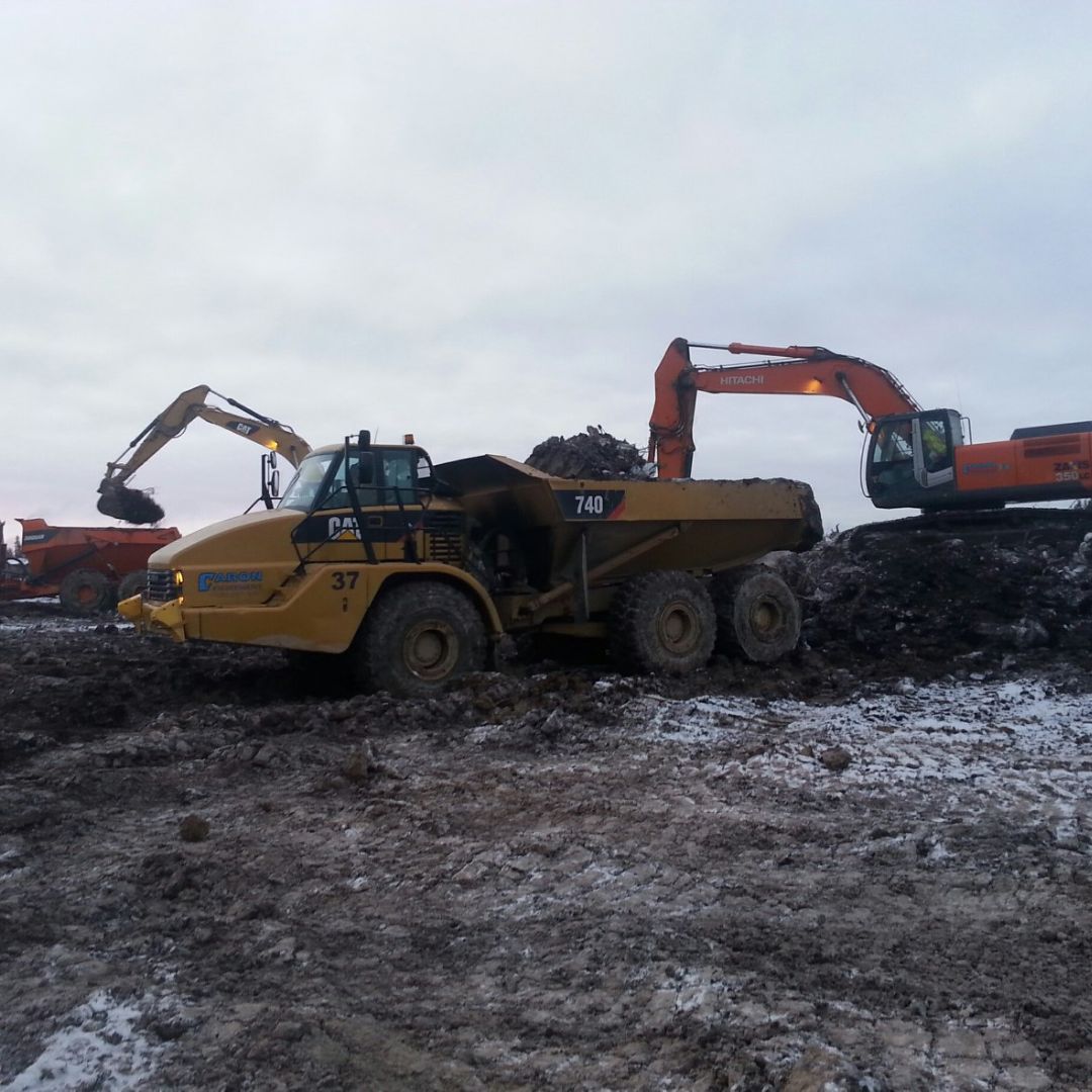 Caron Equipment At a bustling civil construction site, a large yellow dump truck by Caron Equipment and two orange excavators skillfully move earth beneath the cloudy sky.