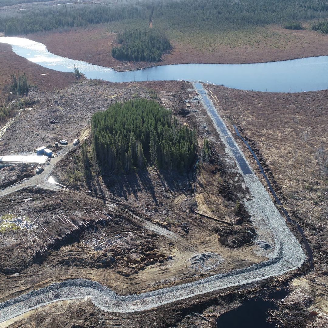 Caron Equipment Aerial view of a winding gravel road through a cleared forest area, reminiscent of Mine Site Construction, with a river in the background.