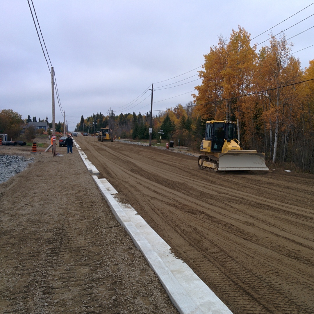 Caron Equipment A bustling civil construction site with bulldozers from Caron Equipment leveling a dirt road framed by autumn trees. Workers in safety vests diligently work while utility poles stretch along one side, ensuring the seamless progress of this project.