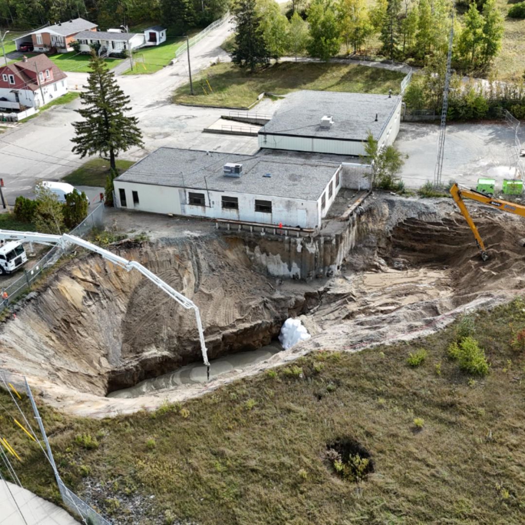 Caron Equipment Aerial view of a construction site featuring extensive excavation work characteristic of mine site construction, adjacent to a small building. Machinery and vehicles, possibly from Caron Equipment, are strategically positioned around the dig.