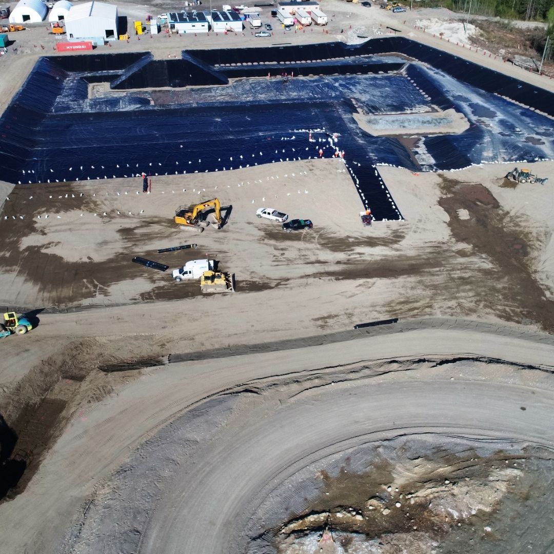 Caron Equipment Aerial view of a mine site construction with black liner installations, excavation equipment, and Caron Equipment vehicles on a dirt surface.