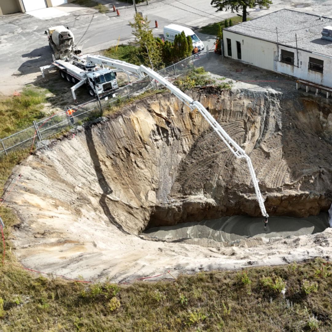 Caron Equipment At a bustling civil construction site, a concrete truck from Caron Equipment skillfully pours concrete into the deep excavation using its long boom arm. Nearby, a portable building and safety barriers ensure that the site's operations run smoothly and safely.