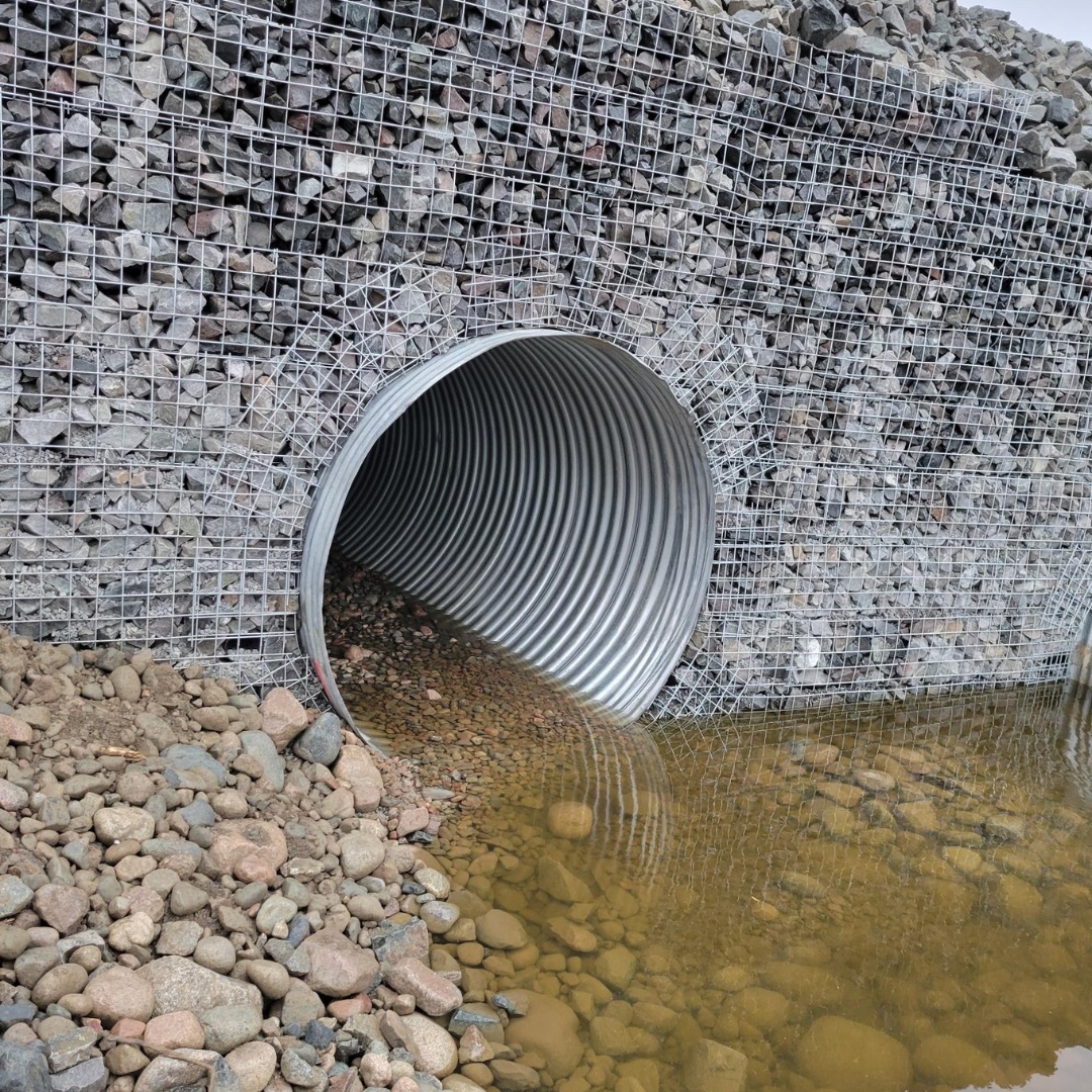 Caron Equipment Corrugated metal culvert with riprap rock surround, partially filled with water, and gravel scattered in front, showcasing Caron Equipment's expertise in civil construction at a mine site.