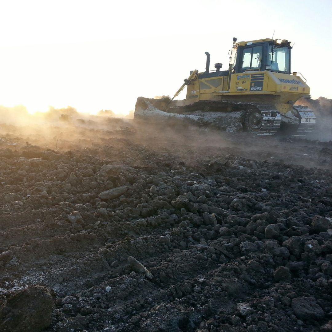 Caron Equipment A bulldozer from Caron Equipment moves earth on a dusty civil construction site, silhouetted against the sunlight in the background.